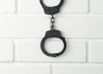 Metal police handcuffs on white painted brick wall