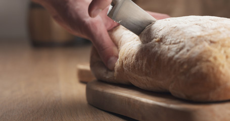 young man hands slicing ciabatta on cutting board