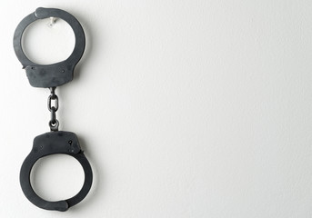 Metal police handcuffs on white painted wall with potential copy space - obrazy, fototapety, plakaty