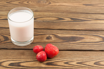Strawberry yogurt in glass and single ripe strawberry on old wooden background