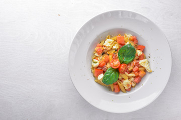 Pasta with vegetables, basil and Parmesan cheese. Italian food. On a wooden background. Top view. Free space for text.