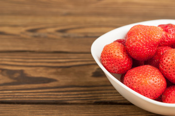 Fresh strawberries in bowl on old wooden planks
