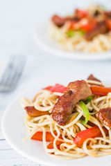 Stir fried spicy pork with red pepper and green onion on white wooden table. Close up