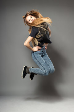 Happy attractive joyful dance model is jumping in studio, isolated on gray background