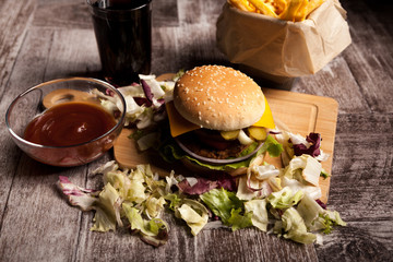 Delicious home made burgers on wooden plate next to fries and cola. Fast food. Unhealthy snack