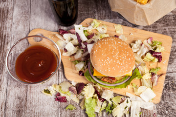 Burger on wooden plate next to fries. Fast food. Unhealthy snack
