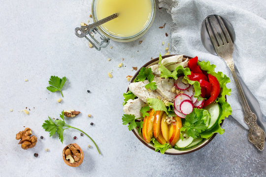 Summer lettuce with salad dressing vinaigrette. Salad with chicken, fresh vegetables, walnuts and greens on a gray stone background or slate. Top view. Copy space.
