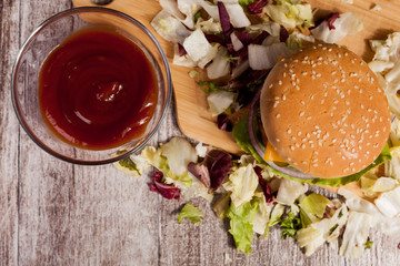 Over top view of delicious home made burger on wooden plate next to fries. Fast food. Unhealthy snack