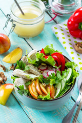 Summer lettuce with salad dressing vinaigrette. Salad with chicken, fresh vegetables, nectarine, walnuts and herbs on a kitchen wooden table.