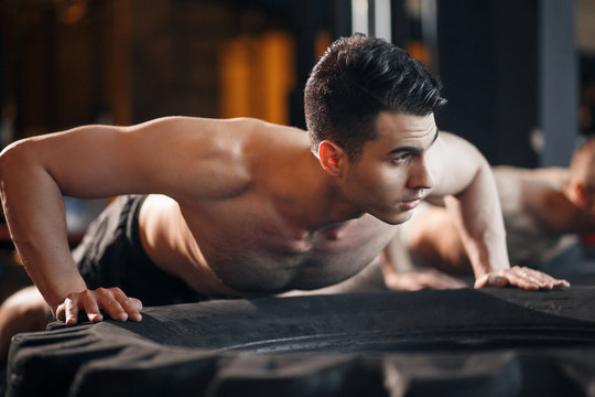 Small group of people doing push-ups on tire. Young athletes working out on beach during a hot summer day.