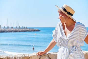 Beautiful girl in a summer dress and hat on the seashore near a background old city europe. Mediterranean Sea, Sitges, Spain