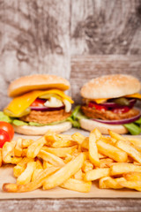 Delicious home made sandwich burgers on wooden plate next to fries. Fast food. Unhealthy snack