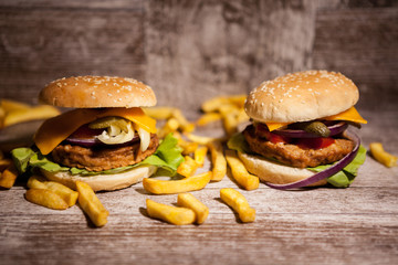Delicious home made sandwich burgers on wooden plate next to fries. Fast food. Unhealthy snack