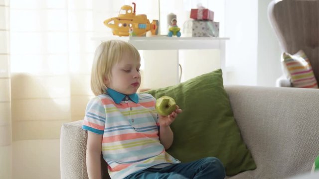 small kid boy bite juicy fresh green apple as a healthy snack during playing at home, wishing to be strong and active