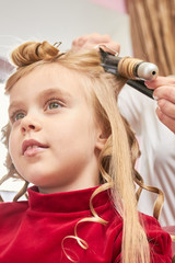 Little girl and curling iron. Child at hairdresser close up.