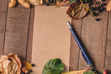 Frame of bright autumn leaves on the boards with a blank page and red apple and blue pen