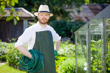 smiling professional young man standing and holding garden hose