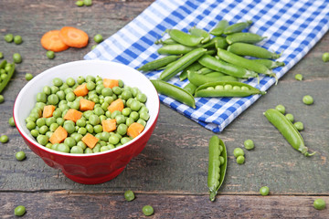 Green peas and carrots sliced in bowl on wooden table