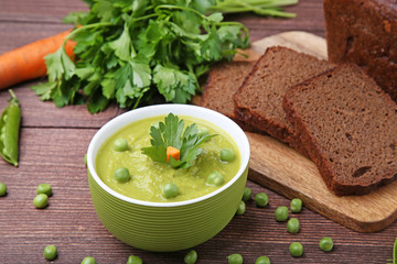 Green peas soup in bowl with bread on wooden table