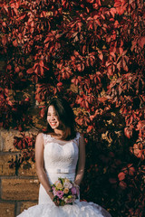 Bride stands by the wall with red leaves
