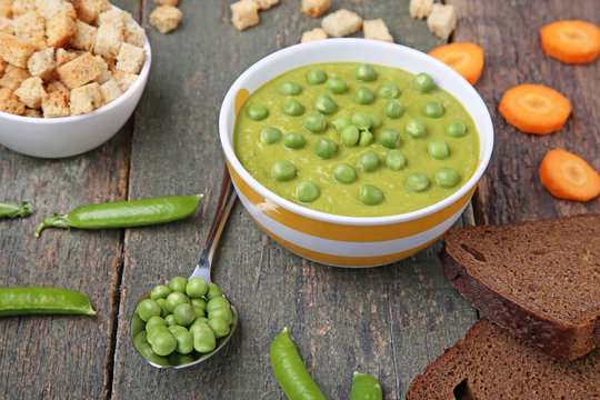 Green peas soup in bowl with rusks on wooden table