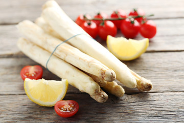 Fresh white asparagus with lemon and tomatoes on a grey wooden table