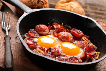 Fried eggs with sausage and onion on frying pan
