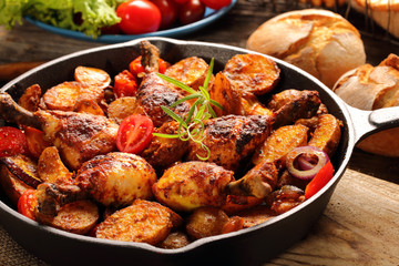 Roasted chicken legs with baked potato on frying pan