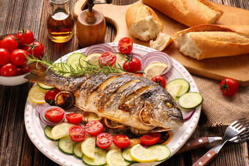 Roasted dorada fish with vegetables on wooden background