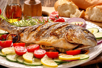 Roasted dorada fish with vegetables on wooden background