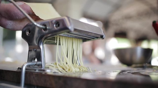 Chef's hands use a pasta cutting machine. Fresh spaghetti pasta coming out of pasta machine close-up, slow mo