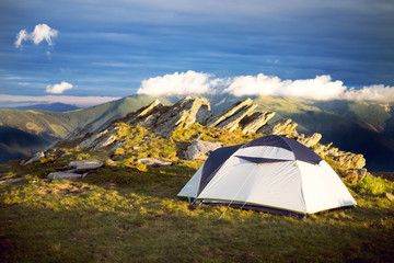 Tourist tent on a grass and next to the rocks. Tent in the mountains. Sunset. Holiday and summer time.