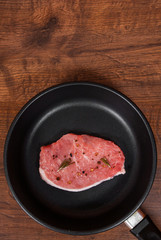 raw meat steak on cast iron frying pan on the brown wooden table background. rustic kitchen table with copy space. top view.