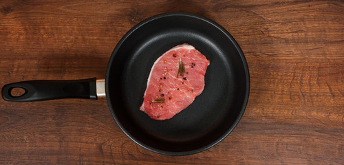 raw meat steak on cast iron frying pan on the brown wooden table background. rustic kitchen table with copy space. top view.