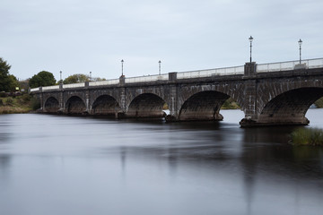 Fototapeta na wymiar Stone bridge with arches over slow flowing river