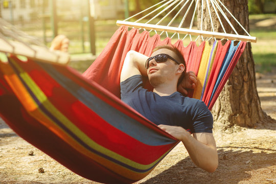 Caucasian man with sunglasses lying on hammock in a pine forest. Outdoors relaxation.