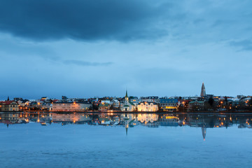 Beautiful reflection of the cityscape of Reykjavik in lake Tjornin at the blue hour in winter with dark clouds