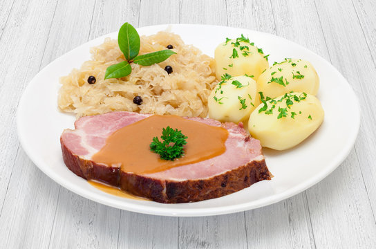 Kasselerbraten mit Sauerkraut und Salzkartoffeln - Tellergericht auf wei&szlig;em Holzuntergrund