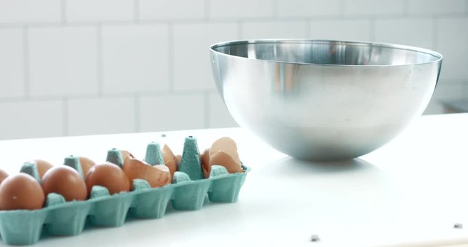 mixed race baker makes a cpan movement of camera showing table with eggs and a bowl ready to make a cake in sunny spaceake. smash eggs