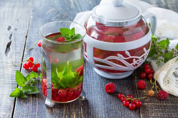 Fruit berry tea with mint, red currant and raspberries on a wooden kitchen table.