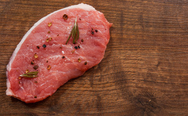raw pork meat chop steak on the brown wooden table background. rustic kitchen table with copy space. top view.