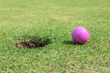 Pink golf ball on green grass near hole