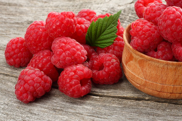 ripe raspberries in wooden bowl on old wooden background