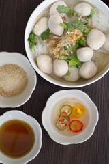 White noodle with pork ball soup in white bowl with seasoning on brown wooden floor  thai food / Still Life food, selective focus
