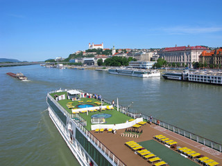 People travel on Danube river on large cruise ship. They looking at panorana of Bratislava city. On hill above the city is Bratislava castle.