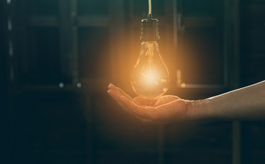Hand of person holding light bulb for idea or success or solar energy - obrazy, fototapety, plakaty