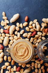 Peanut butter jar and heap of nuts on rustic table top view. © juliasudnitskaya