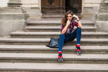 Beauty stylish young woman in dress sitting on steps in sunny bright summer day travel