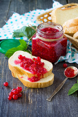 Homemade jam. A glass jar with red currant jam and white bread on a kitchen wooden table. Preserved berry.