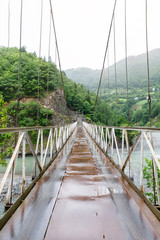 Fototapeta na wymiar Road Suspension bridge over a mountain river during a rain in Georgia